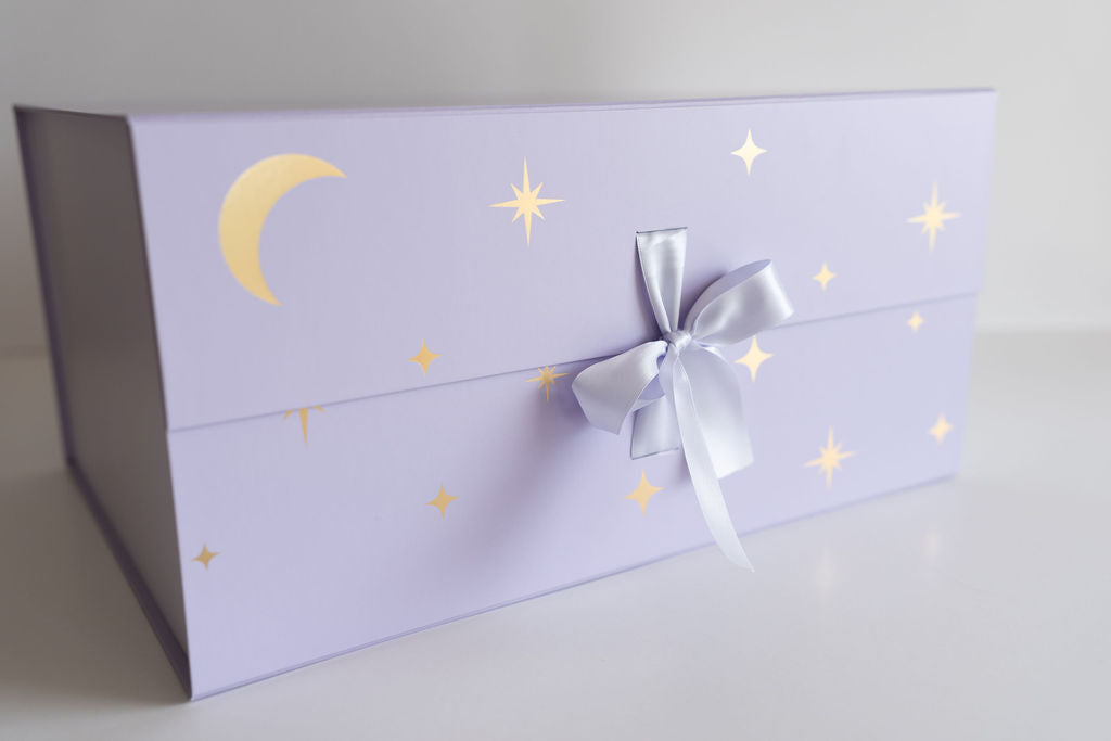 Closed purple SnuggleBox tied with a satin ribbon, featuring gold half-moon and star designs, highlighting its premium, reusable packaging.